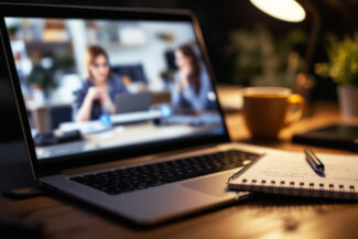 Laptop showing an online lesson next to a notebook and a cup of tea